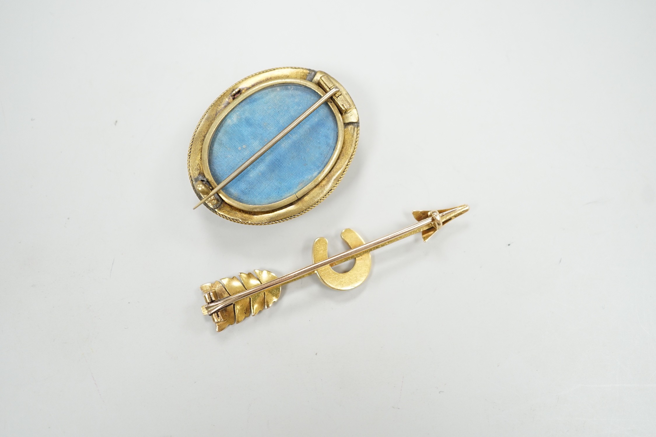 An early 20th century yellow metal, and seed pearl set arrow and horse shoe brooch, 60mm and a Victorian paste set yellow metal oval brooch.